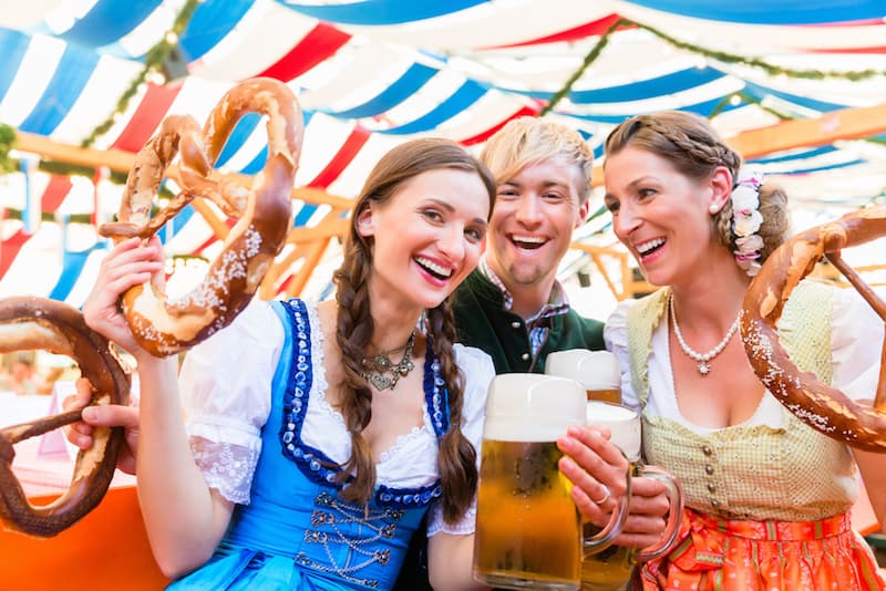 Three people laughing and holding their beer and pretzels during Oktoberfest in Munich