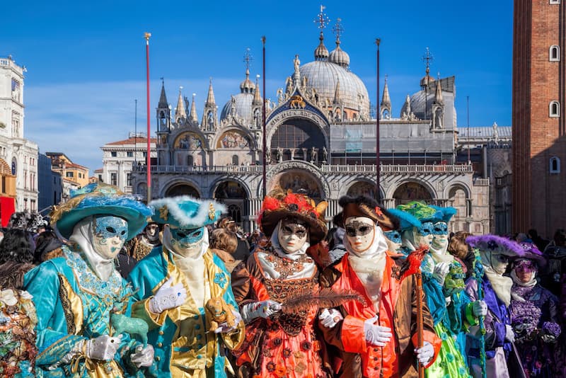 Masked and costumed people celebrating Carnevale outside St. Mark's Basilica in Venice.