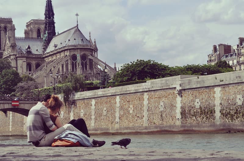 Couple cuddling on the banks of the Seine with a view of the Notre Dame Cathedral in Paris.