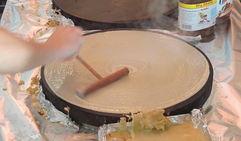 Person spreading the batter on a skillet to start making a crepe