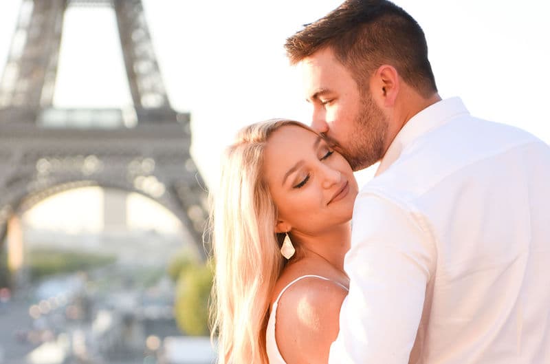 A man and woman embracing in a romantic photo in front of the Eiffel Tower